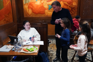Tim Talen, standing with two grandchildren, talking to a student, sitting in a booth with papers and a laptop, studying at Union South.